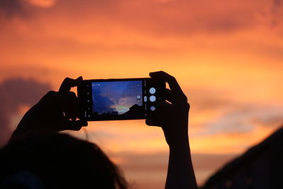 Low angle view of woman holding camera against sky during sunset