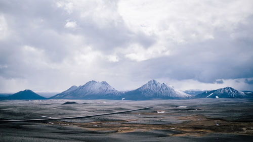 Scenic view of landscape and snowcapped mountains against cloudy sky