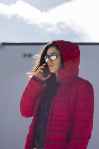 Woman wearing sunglasses and hooded jacket while using phone during winter