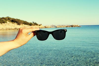 Close-up of hand wearing sunglasses against clear sky