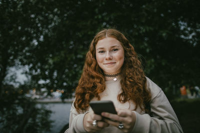 Portrait of smiling teenage girl with long hair holding smart phone