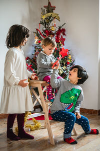 Three children playing next to christmas tree