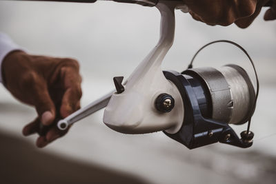 Crop anonymous man turning metal handle of special spinning reel standing on coast while fishing in nature on blurred background