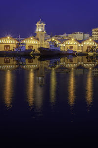 Illuminated city by sea against sky at night