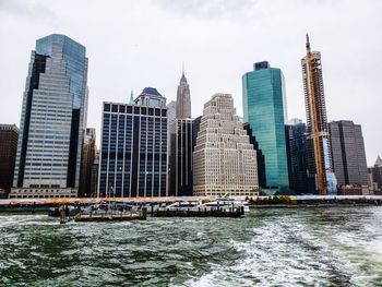 Skyscrapers by river against buildings in city