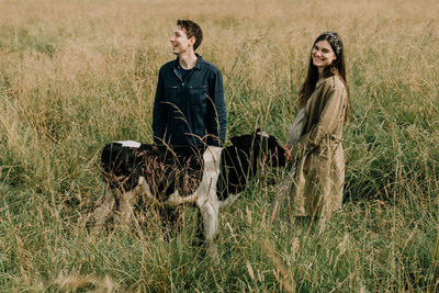 Portrait of pregnant young woman standing with man and calf on grassy land