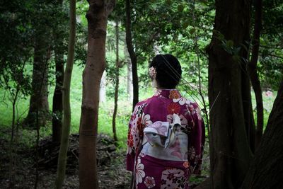 Rear view of woman standing amidst trees in forest