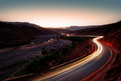 Aerial view of illuminated road by mountains against sky during sunset