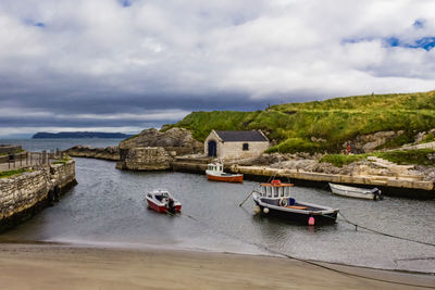 Boats moored at harbor in river against cloudy sky