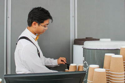 Side view of man taking coffee from machinery in office