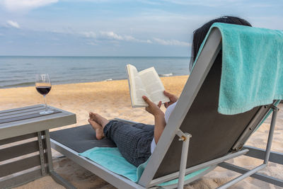 Rear view of woman sitting on chair at beach