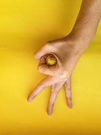 Close-up of human hand gesturing over shiny ball against yellow background