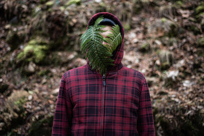 Rear view of man standing in forest with leafs at face