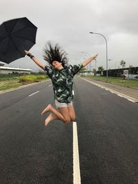 Woman jumping on road against sky