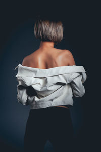 Rear view of seductive woman wearing jacket standing against black background