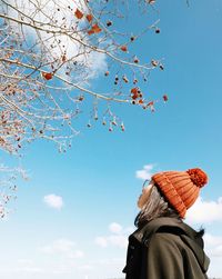 Low angle view of woman looking at tree against sky during winter