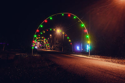 Illuminated ferris wheel against sky in city at night