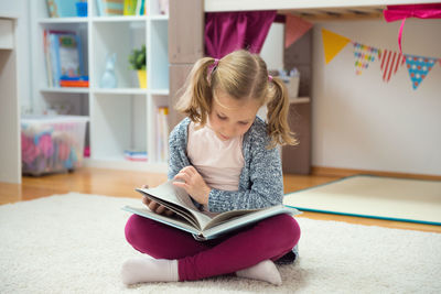 Girl reading book while sitting on carpet at home