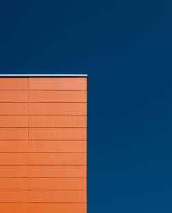 Low angle view of orange building against clear blue sky