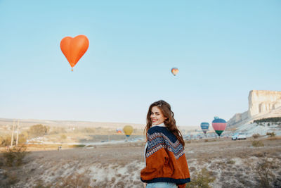 Rear view of woman with balloons on field against clear sky