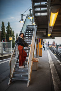 Rear view of woman on railway bridge against sky in city