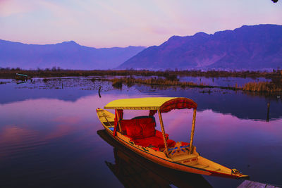 Boat moored by lake against sky during sunset