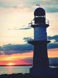 Lighthouse by sea against sky during sunset