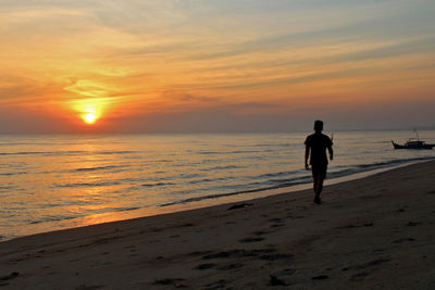 Silhouette man walking at beach against sky during sunset