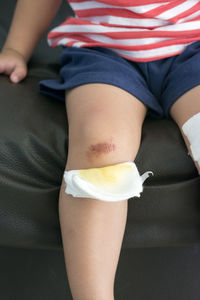 Midsection of boy showing wound while sitting on sofa with bandage on knees