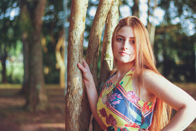 Beautiful young woman looking away while standing by trees in forest