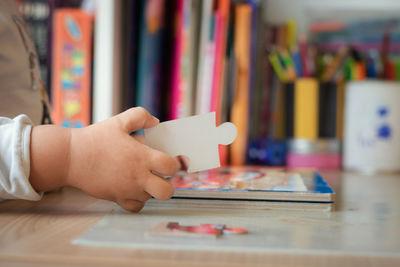 Cropped hand of child holding jigsaw puzzle on table