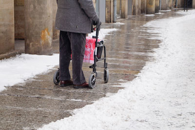 Low section of man standing with mobility walker on footpath in city during winter