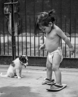 Shirtless toddler wearing flip-flops by puppy in back yard