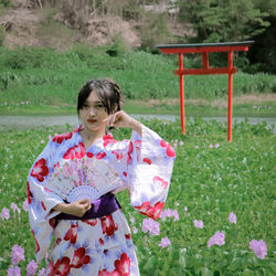 Portrait of woman wearing kimono holding hand fan while standing in park