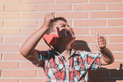 Cheerful boy listening music while standing against wall