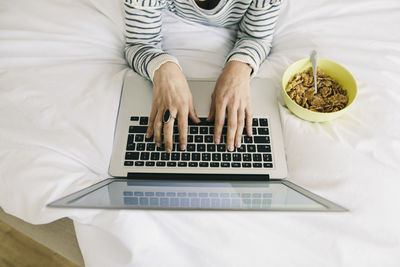 Woman in bed with laptop and muesli bowl