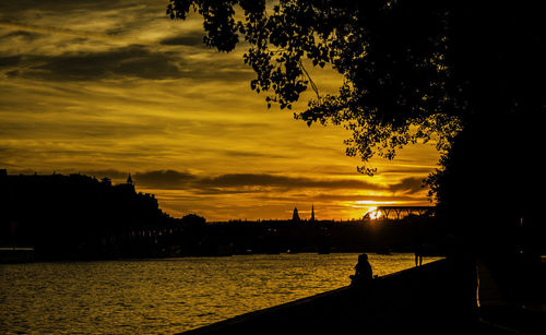 Silhouette trees by river against orange sky