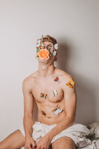 Portrait of shirtless man sitting against wall