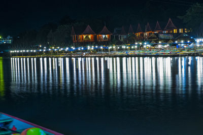 Illuminated buildings by lake against sky at night