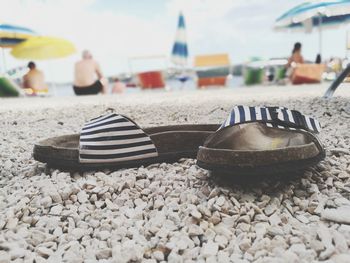 Close-up of slippers on beach against sky