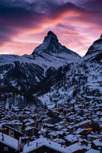 Snow covered houses and mountains against sky during sunset