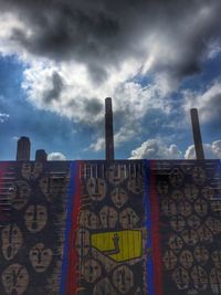 Low angle view of graffiti on wall against cloudy sky