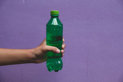 Person holding glass bottle against wall