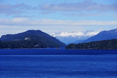 Scenic view of blue river and mountains against cloudy sky