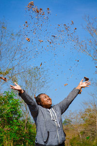 Low angel view of woman throwing autumn leaves outdoors