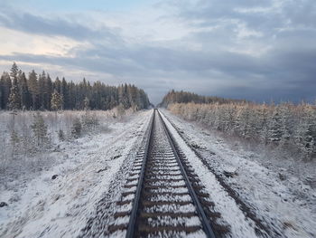 Diminishing perspective of railroad track against cloudy sky during winter