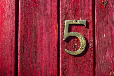 House number 5 on a rough red wooden front door in london 