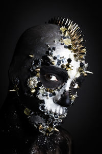 Close-up portrait of man with face paint and ornaments against black background