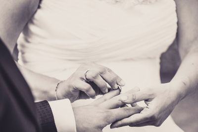 Midsection of bride putting ring in groom finger