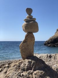 Stack of stones on rock by sea against sky